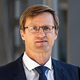 (c) HZDR Mann mit Brille, Anzug und Krawatte, neutralem Gesichtsausdruck, vor einem modernen Hintergrund.